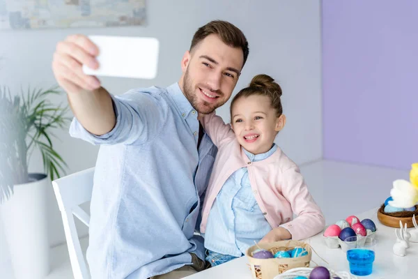 Jovem pai e filha tomando selfie enquanto pinta ovos para a Páscoa — Fotografia de Stock