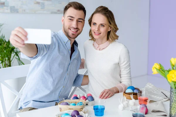 Young man and woman taking selfie while painting Easter eggs — Stock Photo