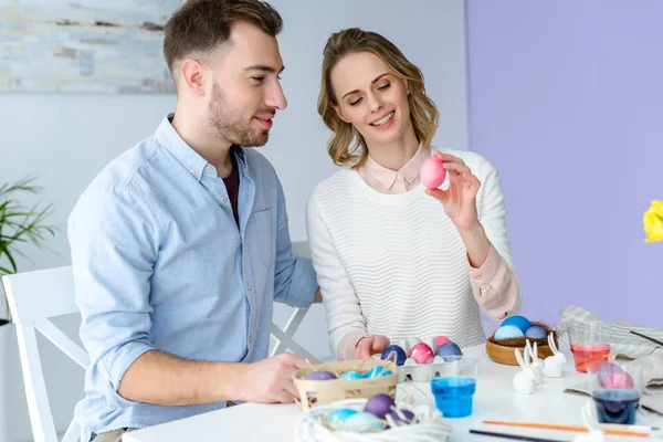 Happy family celebrating Easter with colored eggs on table — Stock Photo