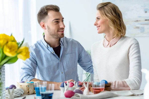 Усміхнена пара за столом з розфарбованими великодніми яйцями — стокове фото