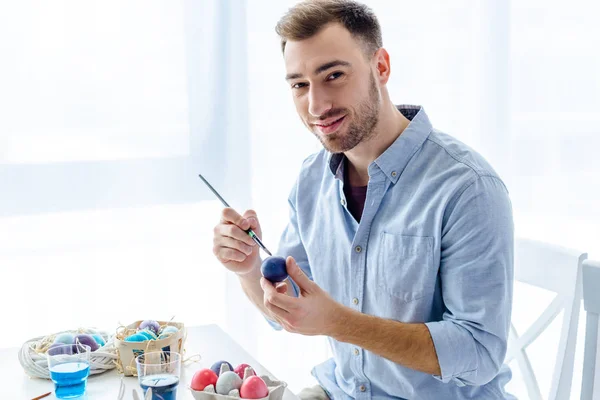 Junger Mann bemalt Ostereier in verschiedenen Farben — Stockfoto