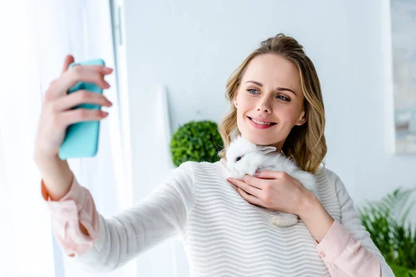 Mujer rubia sosteniendo conejo blanco y tomando selfie - foto de stock