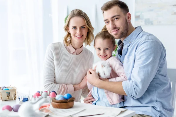 Glückliche Familie hält Osterhasen mit Ostereiern auf dem Tisch — Stock Photo