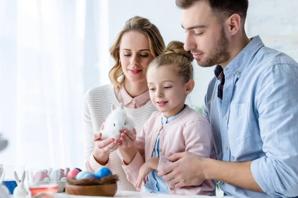 Family playing with Easter rabbit by table with painted eggs — Stock Photo