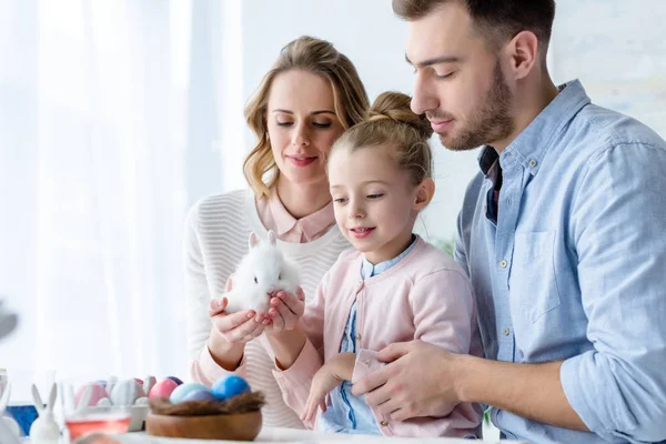 Família brincando com coelho de Páscoa por mesa com ovos pintados — Fotografia de Stock