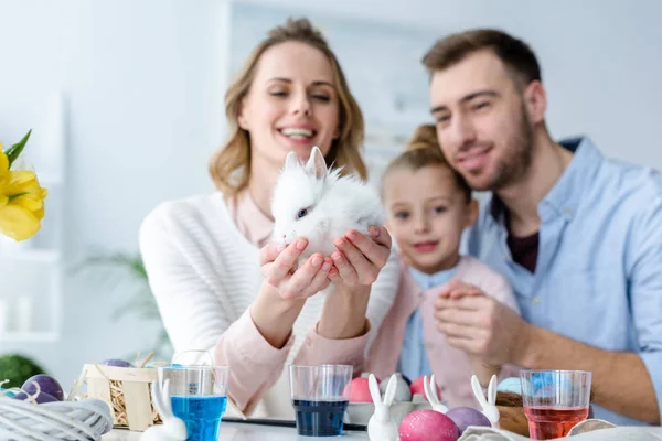 Mother with family holding cute bunny by table with Easter eggs — Stock Photo