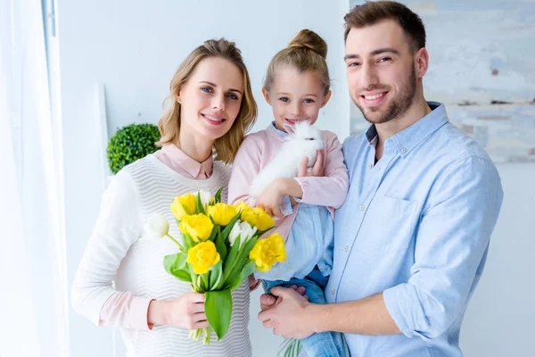 Cute daughter holding bunny while mother holding tulips — Stock Photo