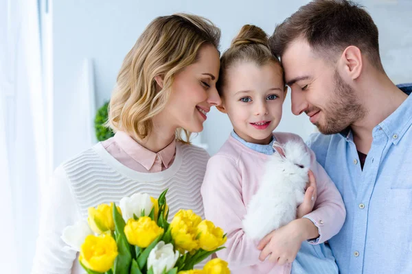 Familia feliz con lindo conejito y flores de primavera - foto de stock