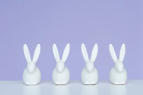 Rabbit statuettes in row on violet background — Stock Photo