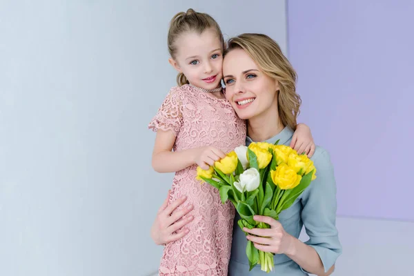 Mujer sosteniendo ramo y abrazando linda hija en el día de la mujer - foto de stock