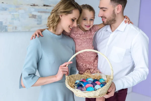 Усміхнена сім'я тримає кошик з розфарбованими великодніми яйцями — стокове фото