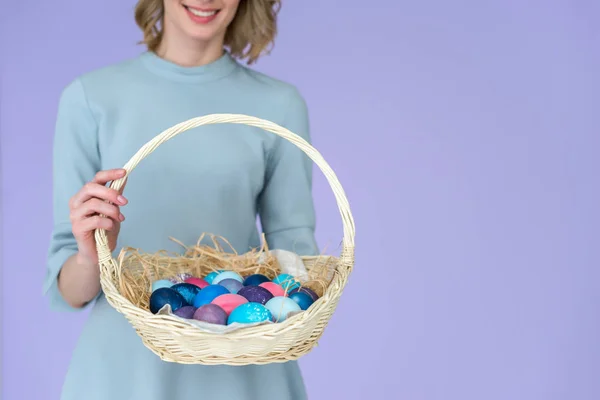 Vue rapprochée de la femme aux œufs peints dans le panier de Pâques œufs colorés isolés sur violet — Photo de stock