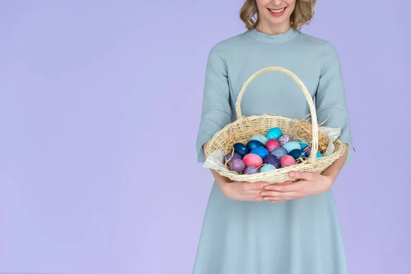 Woman with painted Easter eggs in basket isolated on violet — Stock Photo