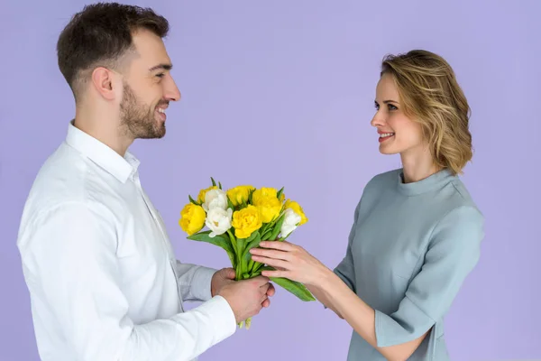 Man presenting bouquet of tulips to woman on women's day isolated on violet — Stock Photo