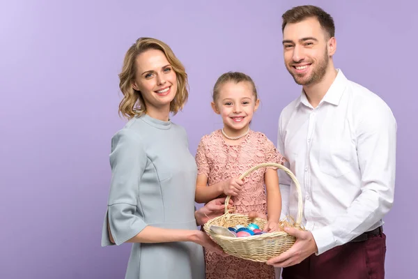 Genitori e figlia con cesto pasquale con uova colorate isolate su viola — Foto stock