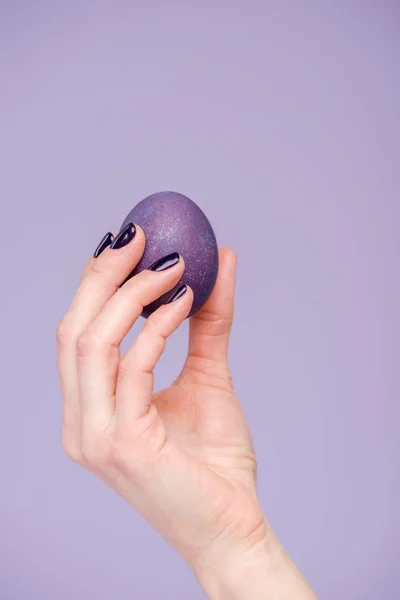 Mano femminile con uovo di Pasqua viola isolato su viola — Foto stock