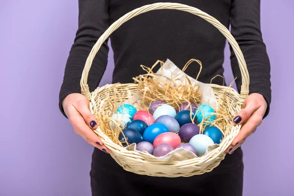 Femme avec des œufs de Pâques colorés dans le panier isolé sur violet — Photo de stock
