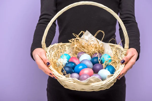 Woman with colored Easter eggs in basket isolated on violet — Stock Photo