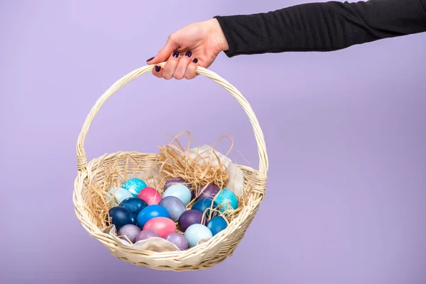 Femme tenant panier de Pâques avec des œufs colorés isolés sur violet — Photo de stock