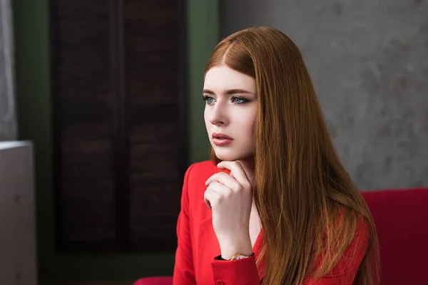 Молода жіноча модель, одягнена в червону куртку, тримає палець на підборідді — стокове фото