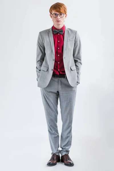 Male fashion model in eyeglasses dressed in suit and bow tie isolated on grey — Stock Photo