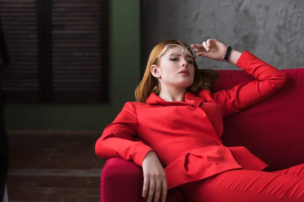 Stylish young woman taking off eyeglasses and lying on couch — Stock Photo