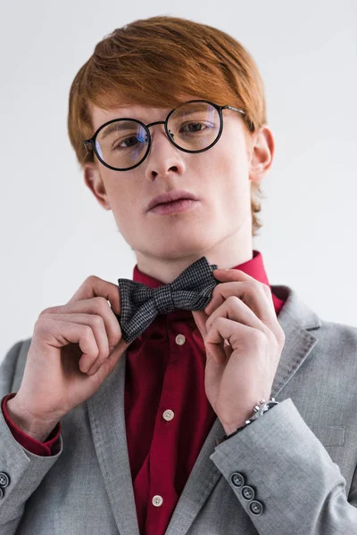 Low angle view of male fashion model in eyeglasses adjusting bow tie isolated on grey — Stock Photo