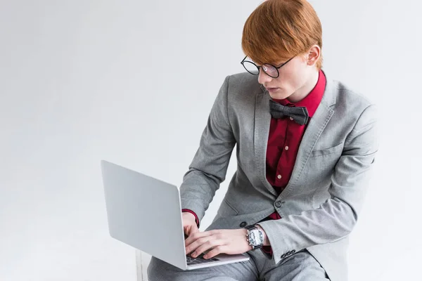 Male fashion model dressed in suit using laptop isolated on grey — Stock Photo