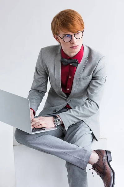 Young male fashion model in eyeglasses using laptop isolated on grey — Stock Photo