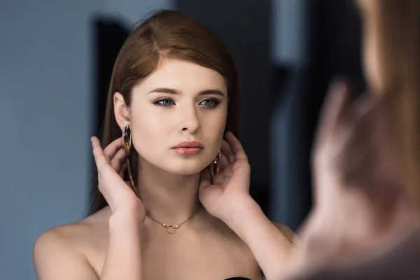 Young stylish female model with earrings looking at own reflection — Stock Photo