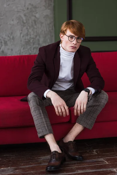 Male model in eyeglasses dressed in jacket sitting on couch — Stock Photo