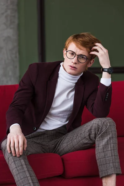 Portrait of young male fashion model in eyeglasses sitting on couch — Stock Photo