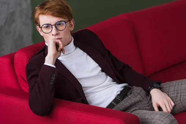 Jovem modelo de moda masculina em óculos sentados no sofá — Fotografia de Stock