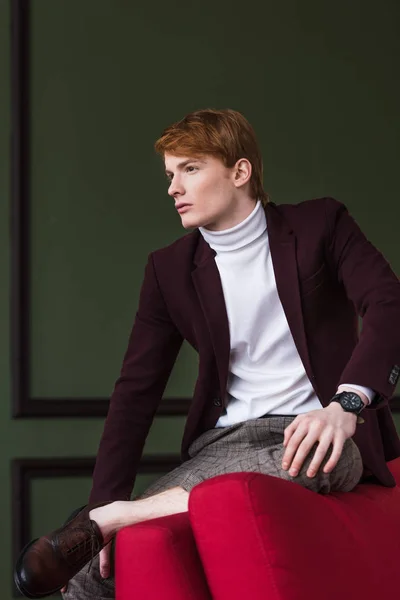 Vista lateral do jovem modelo de moda masculina sentado na borda do sofá — Fotografia de Stock