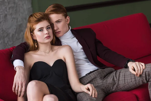 Joven modelo de moda femenina con pendientes y collar sentado con novio en el sofá - foto de stock