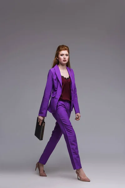 Female fashion model in suit carrying handbag isolated on grey — Stock Photo