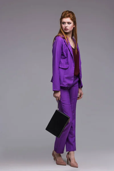 Young female fashion model in suit holding hanbag isolated on grey — Stock Photo