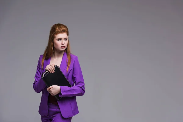 Молода жіноча модель моди в фіолетовому костюмі тримає сумку ізольовано на сірому — стокове фото