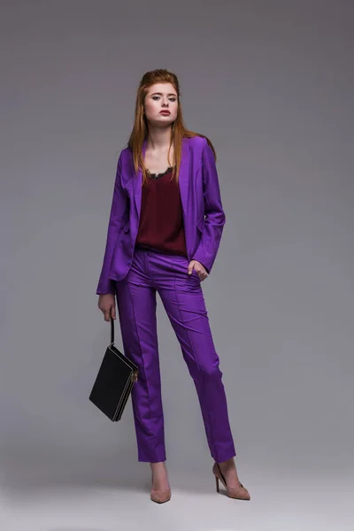 Junge weibliche Mode-Modell in formalen Anzug hält Handtasche isoliert auf grau — Stockfoto