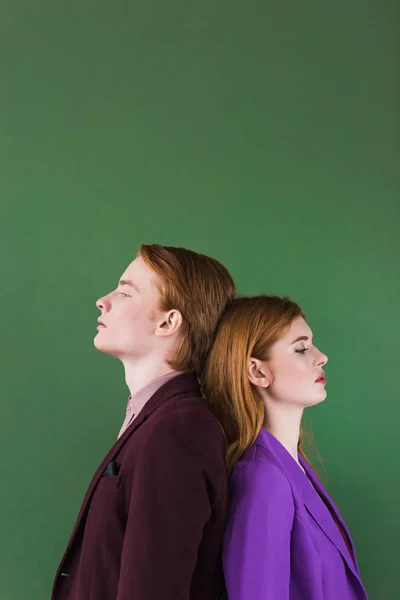 Vue latérale du couple élégant de modèles debout dos à dos isolé sur le vert — Photo de stock