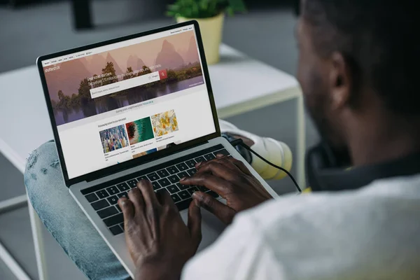 Plan recadré de jeune homme afro-américain en utilisant un ordinateur portable avec le site shutterstock à l'écran — Photo de stock