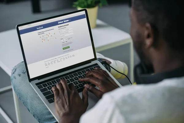 Cropped shot of young african american man using laptop with facebook website on screen — Stock Photo