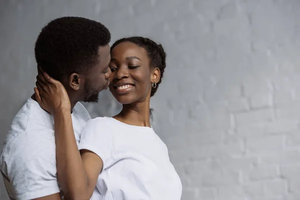 Glückliches junges afrikanisch-amerikanisches Paar in weißen T-Shirts, das sich zu Hause umarmt — Stockfoto