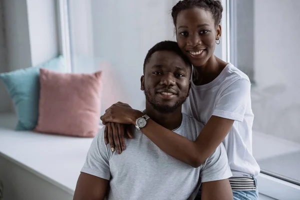 Feliz joven afroamericano pareja en blanco camisetas sonriendo a la cámara en casa — Stock Photo