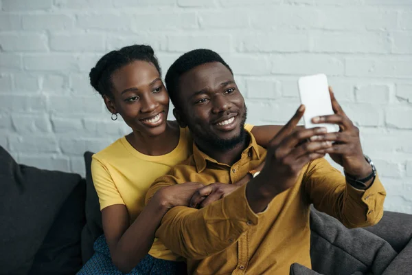 Красивая счастливая молодая африканская пара делает селфи со смартфоном дома — стоковое фото