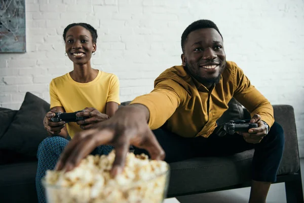 Щаслива молода афроамериканська пара їсть попкорн і грає з джойстиками вдома — стокове фото