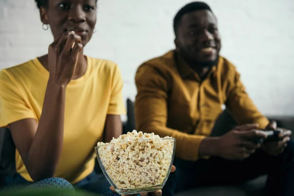 Schnappschuss einer Afroamerikanerin, die Popcorn isst, während ihr Freund zu Hause mit dem Steuerknüppel spielt — Stockfoto