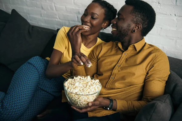 Happy young african american couple eating popcorn while sitting on sofa at home — Stock Photo