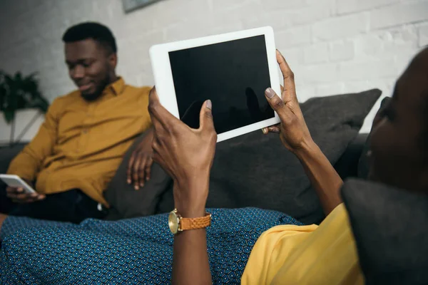 Plan recadré de la jeune femme couchée sur le canapé avec tablette numérique tout en petit ami en utilisant smartphone — Photo de stock