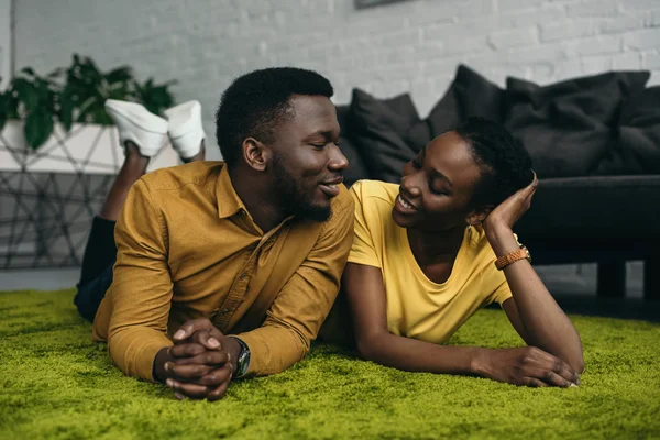 Schönes junges afrikanisch-amerikanisches Paar liegt auf Teppich und lächelt sich zu Hause an — Stockfoto